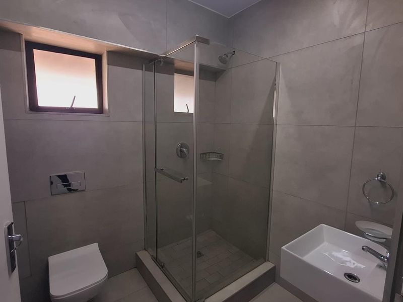 Modern bathroom featuring a wall-mounted toilet, glass shower enclosure, and wall-mounted basin with contemporary large-format tiling throughout.