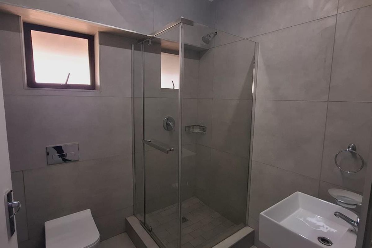 Modern bathroom featuring a wall-mounted toilet, glass shower enclosure, and wall-mounted basin with contemporary large-format tiling throughout.