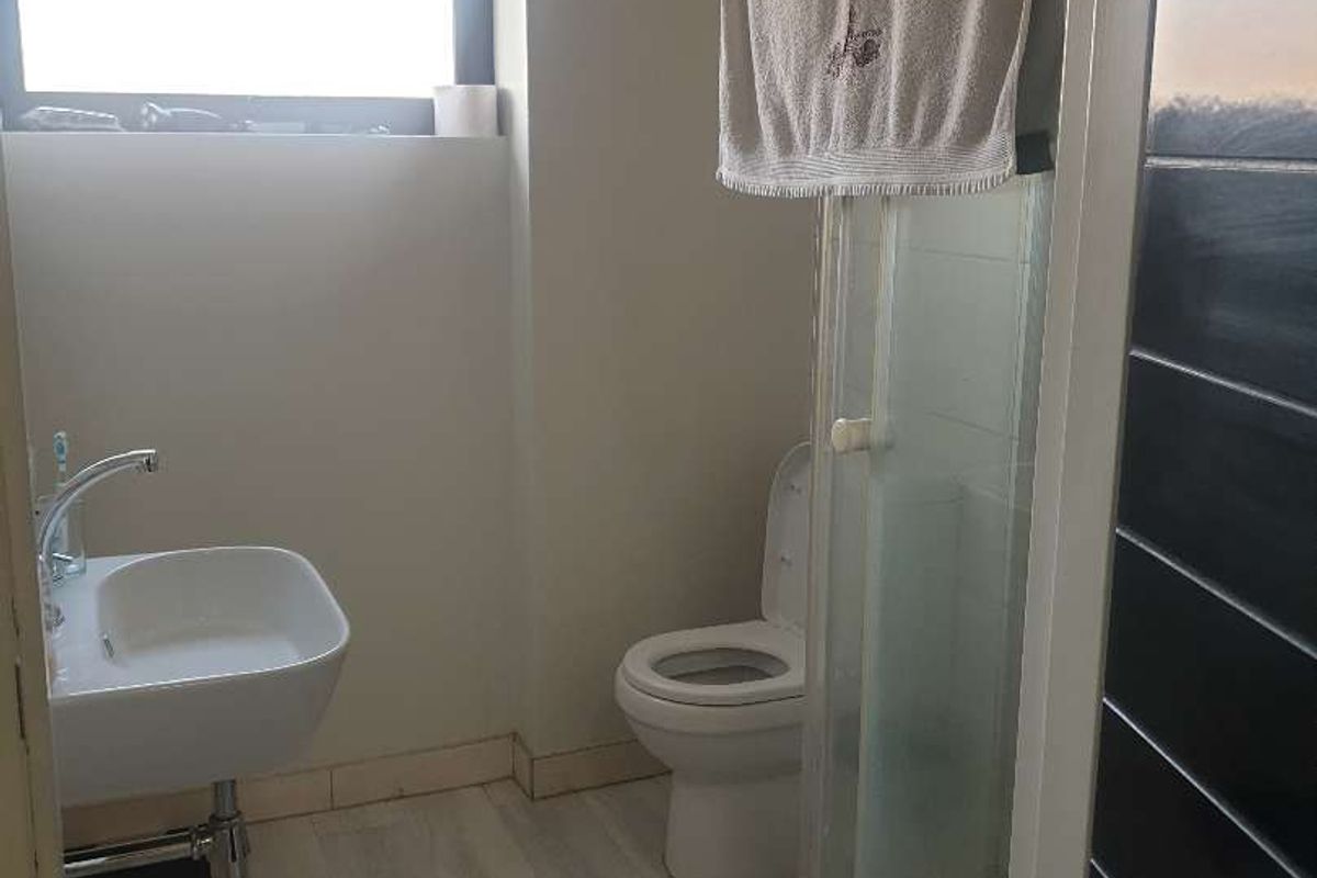 A functional bathroom featuring a glass-enclosed shower, a wall-mounted bidet, and a toilet, finished with light wood-look flooring and dark accent wall tiles.