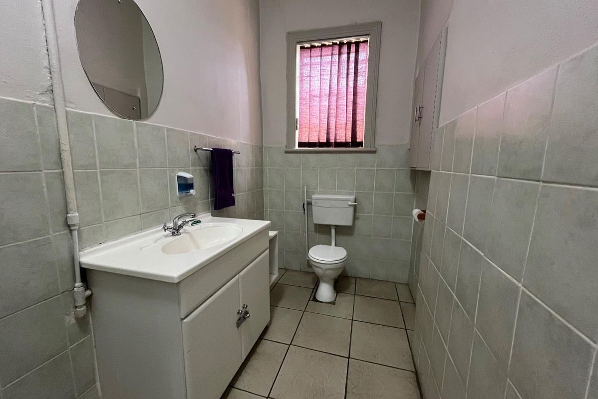 A functional office bathroom featuring a vanity basin, toilet, and tiled walls with a window for natural light.