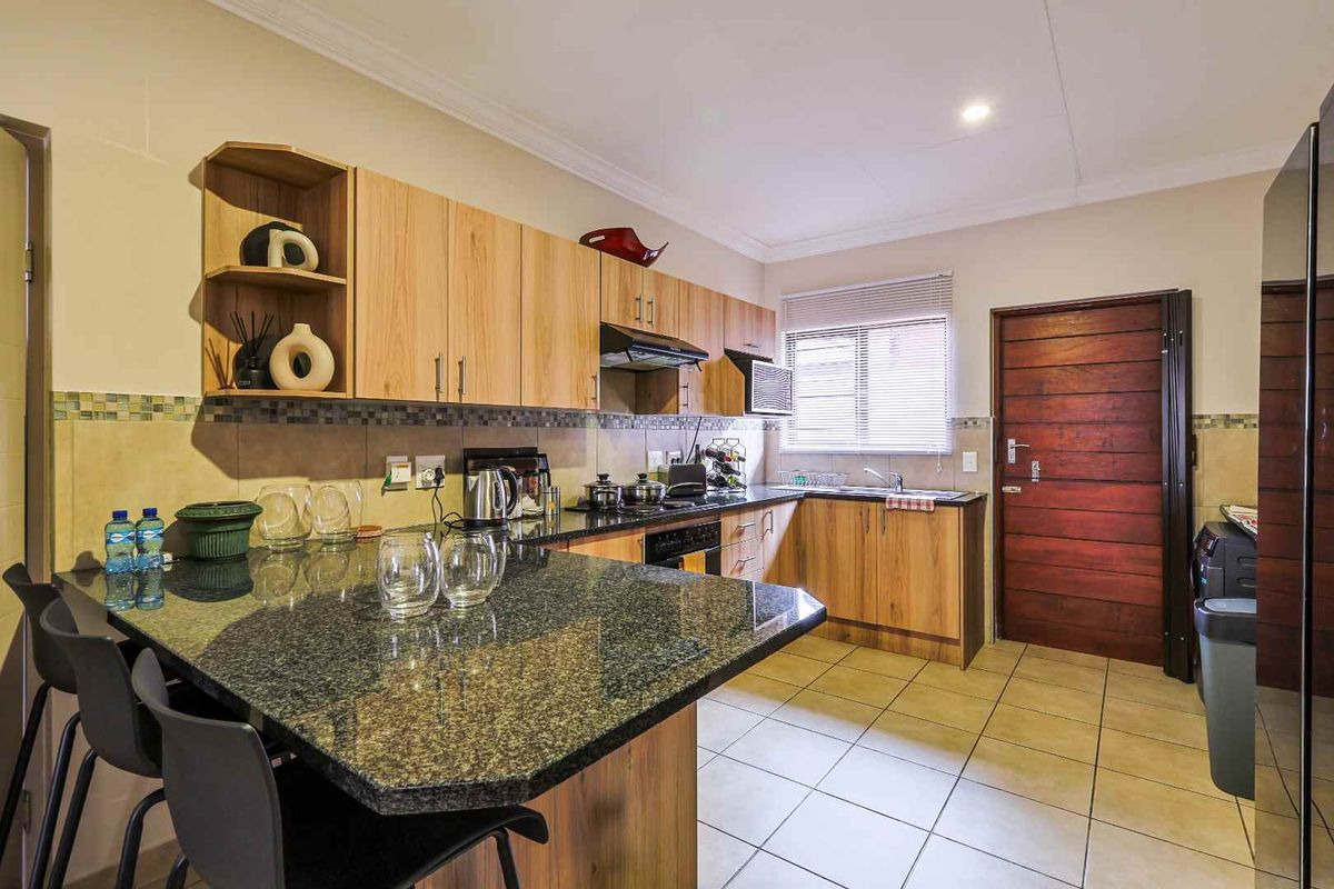 A functional kitchen featuring wood-finish cabinetry, granite countertops, a breakfast bar, tiled flooring, and a built-in oven with an extractor fan.