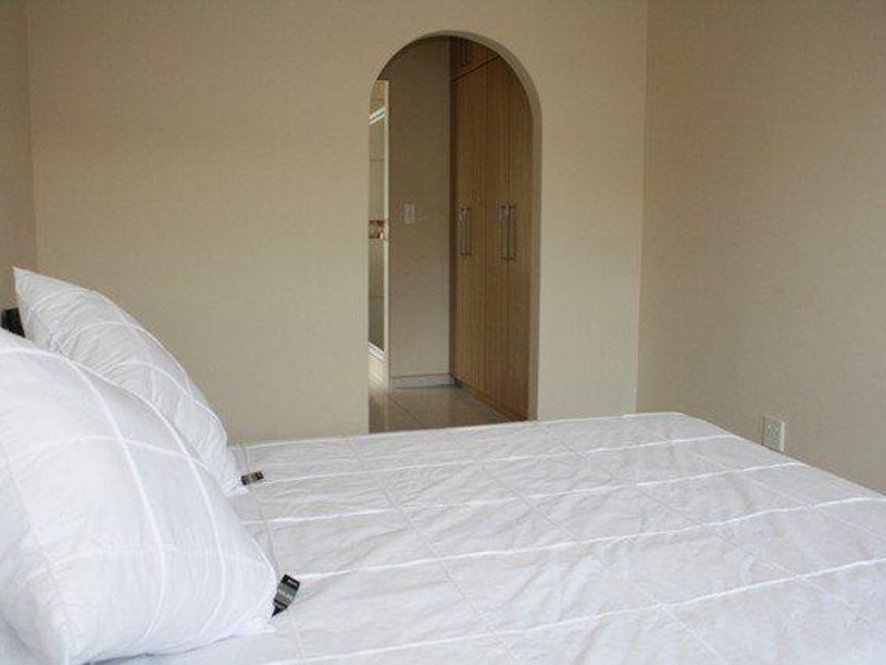 A bedroom featuring neutral walls, built-in wooden cupboards, and an arched doorway leading to an adjacent space.