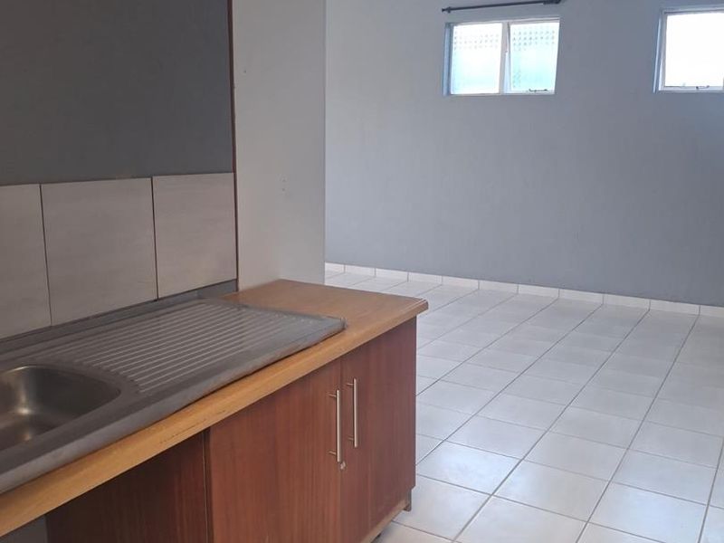 An empty kitchen area featuring tiled flooring, a single sink unit, and basic cabinetry, presenting a blank canvas for potential renovation.