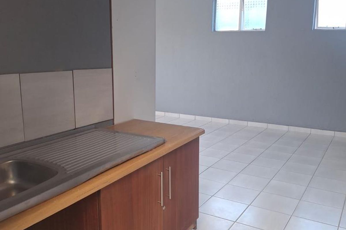 An empty kitchen area featuring tiled flooring, a single sink unit, and basic cabinetry, presenting a blank canvas for potential renovation.