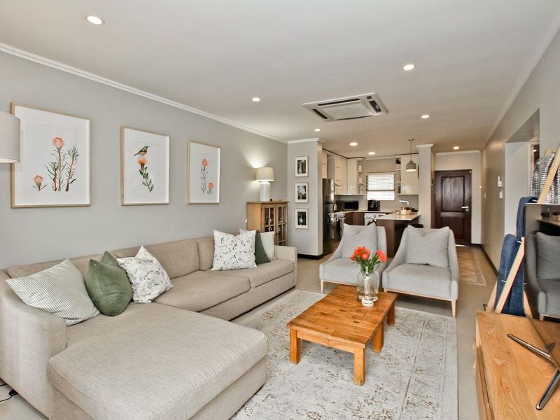 Open-plan living area featuring a modern kitchen with island, integrated appliances, recessed lighting, and ducted air conditioning, flowing into a comfortable lounge space.