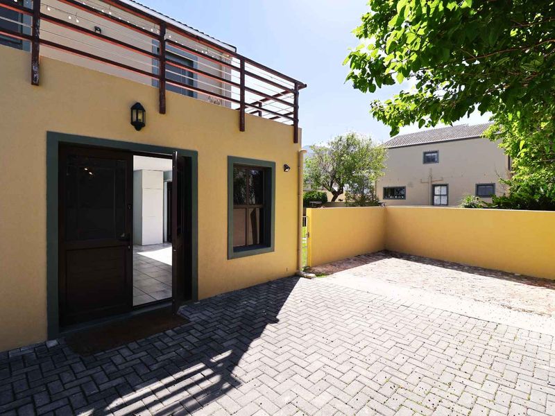 A rear courtyard featuring paved flooring, a boundary wall, and an upper-level balcony with a wooden railing.