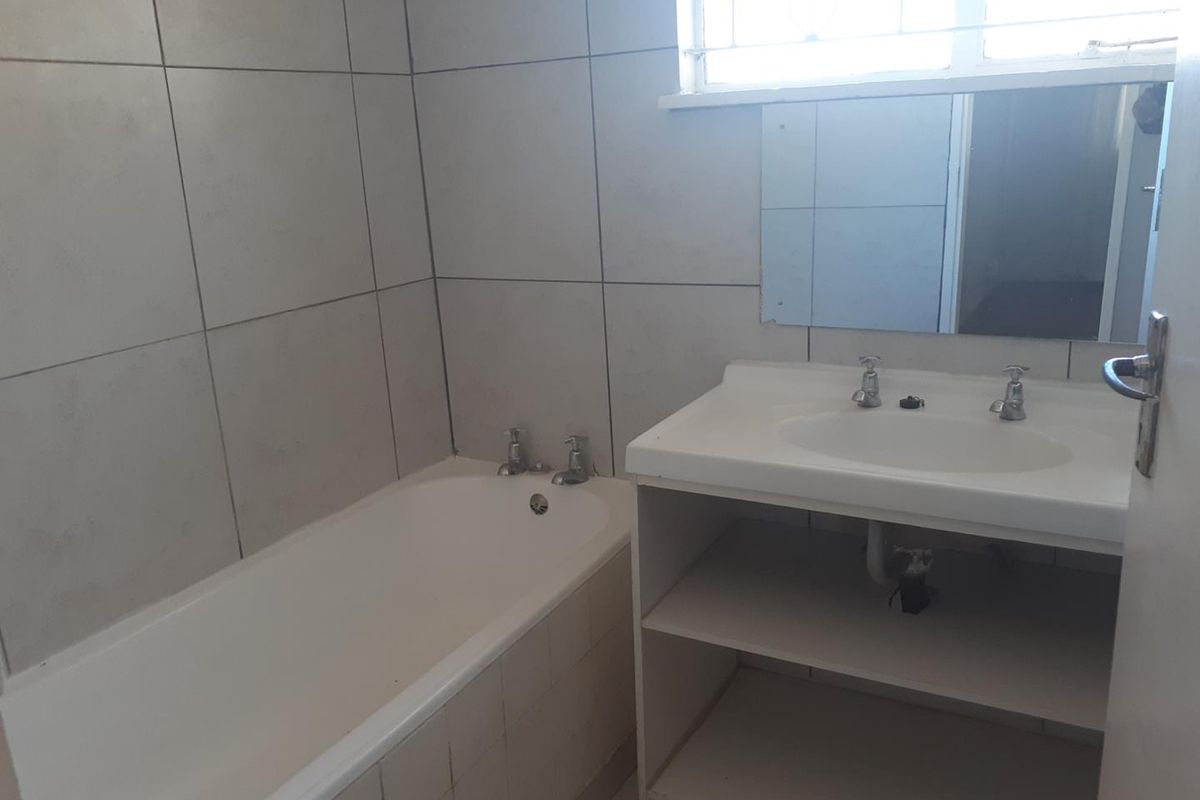 A functional bathroom featuring a built-in bathtub, wall-mounted vanity with integrated basin, and tiled wall finishes.