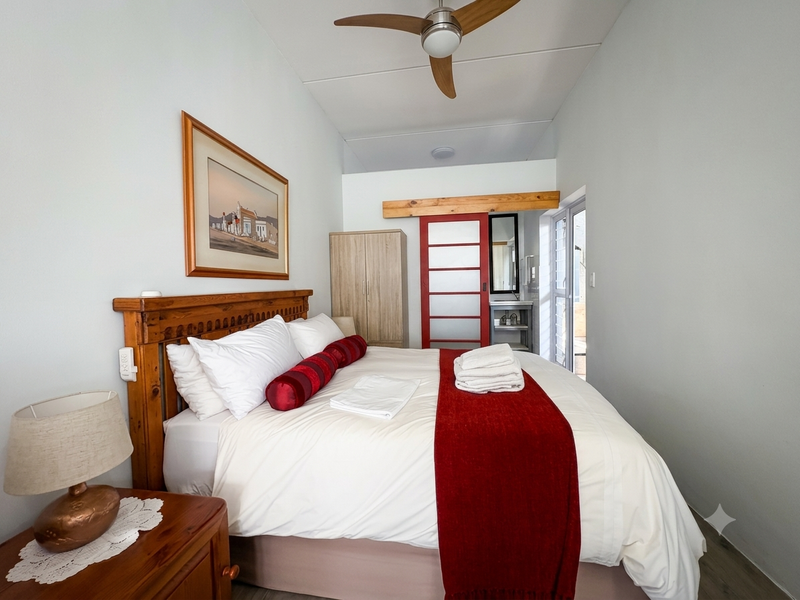 A well-maintained bedroom featuring a ceiling fan, neutral walls, and a sliding door leading to an adjoining vanity area.