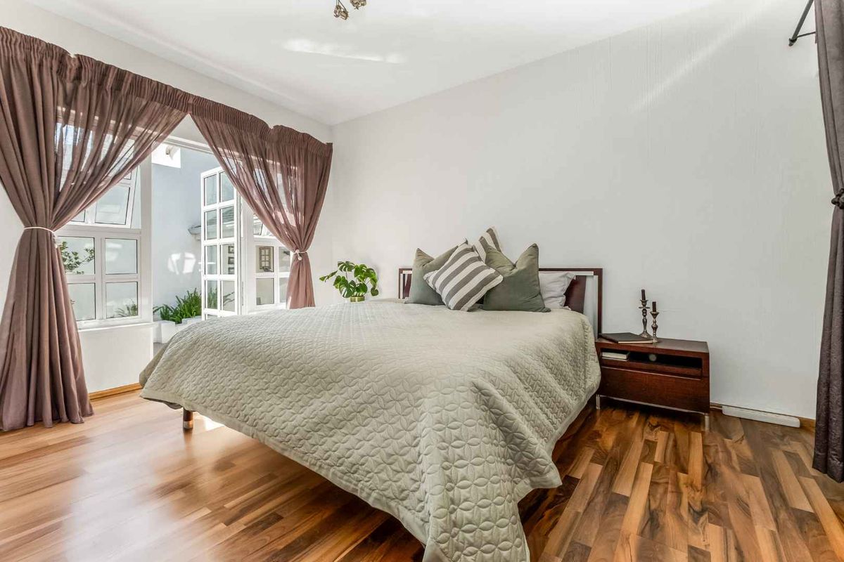 A bright bedroom featuring warm-toned laminate flooring and direct access to an outdoor area through classic french doors.