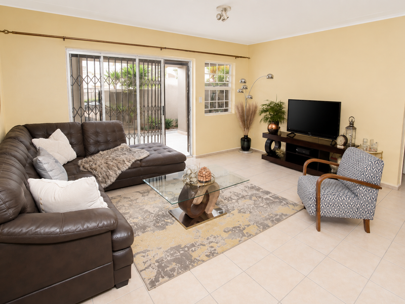 A well-lit living room featuring ceramic floor tiles, neutral walls, and a sliding glass door providing access to the outdoor area.