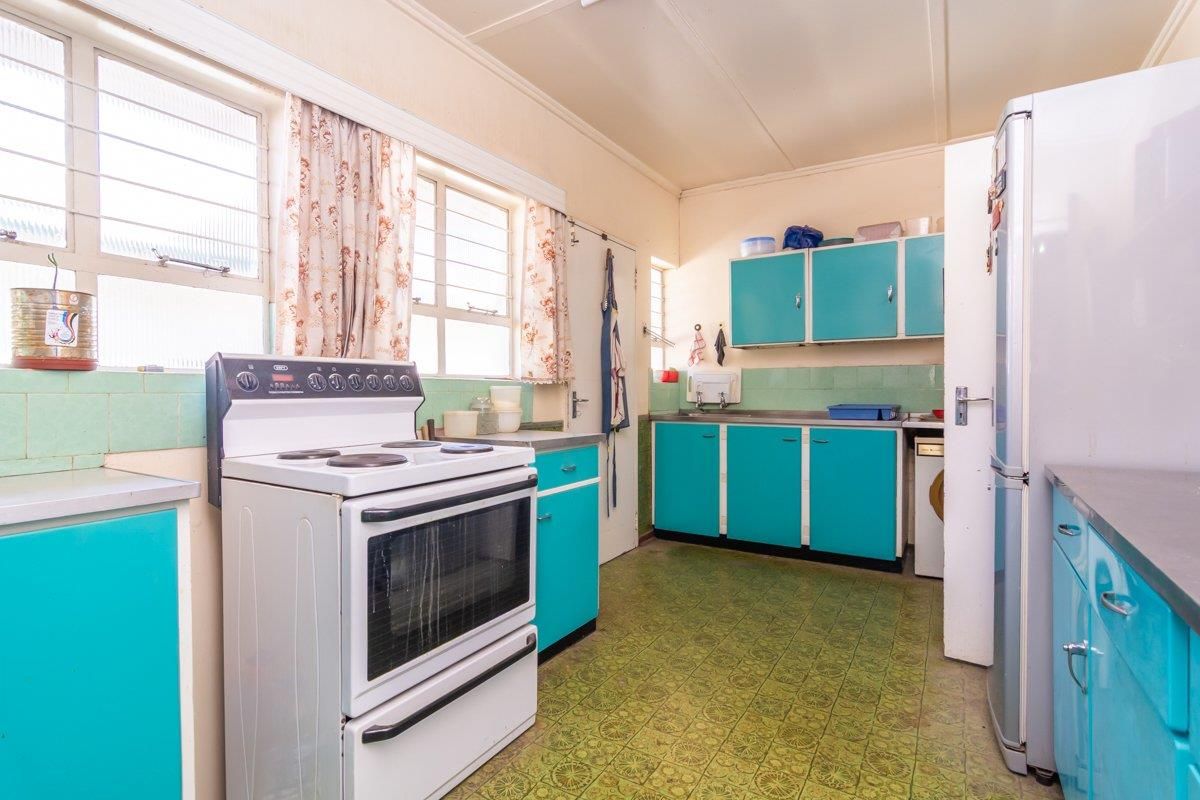 A dated kitchen featuring original cabinetry, a freestanding electric stove, and vintage patterned flooring, offering significant potential for a modern renovation.