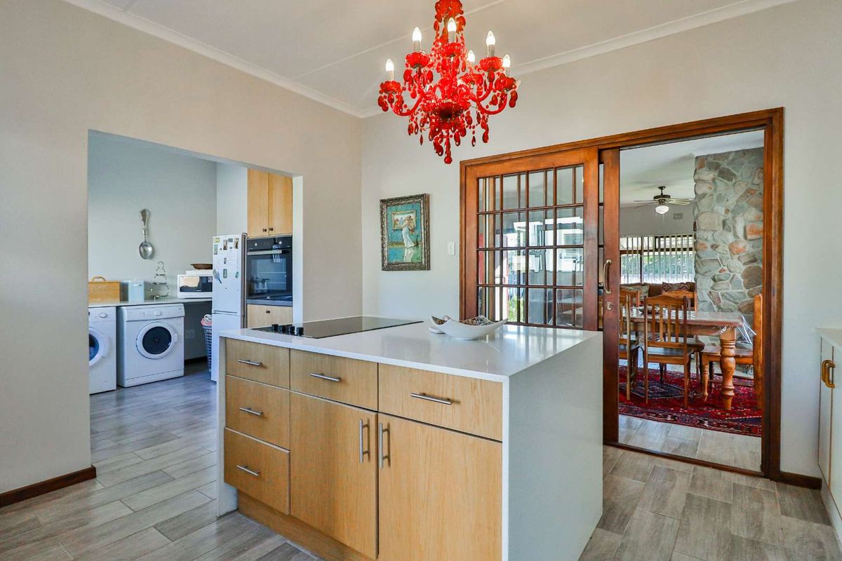 Modern kitchen featuring a central island with a built-in hob, stone countertops, and light wood cabinetry, opening into a laundry area and dining room.