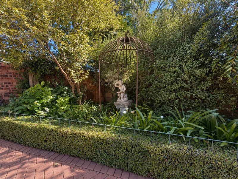 A well-maintained garden area featuring established hedging, brick paving, and a decorative metal garden structure set against a brick boundary wall.