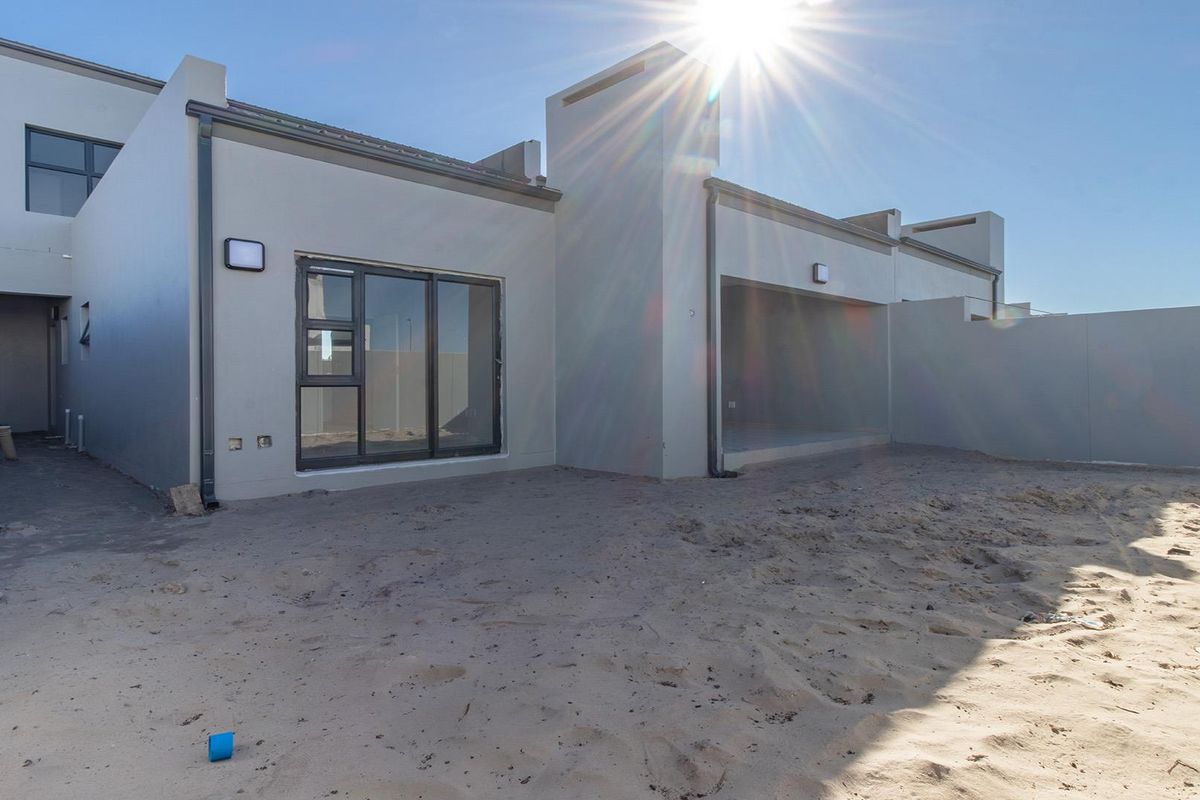Rear view of the property featuring a covered patio area, sliding glass doors, and an expansive, unlandscaped sandy backyard.