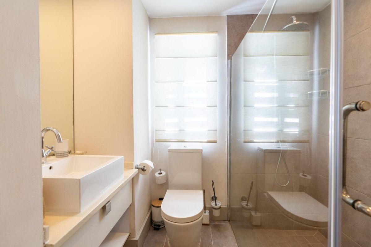 Modern bathroom featuring a glass-enclosed shower, contemporary vanity with basin, and a wall-mounted toilet, finished with neutral tiling and natural light.