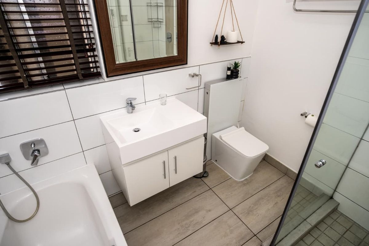 Modern bathroom featuring a vanity basin, concealed cistern toilet, bathtub with handheld shower, and a separate glass-enclosed shower area with contemporary tiling.