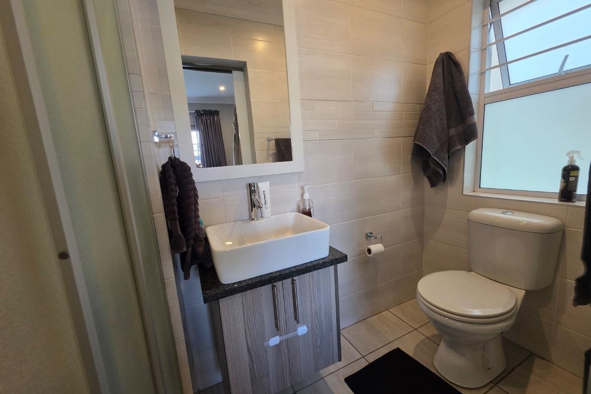 A compact, modern bathroom featuring a vessel sink vanity, wall-mounted mirror, and a standard toilet with neutral wall and floor tiling.