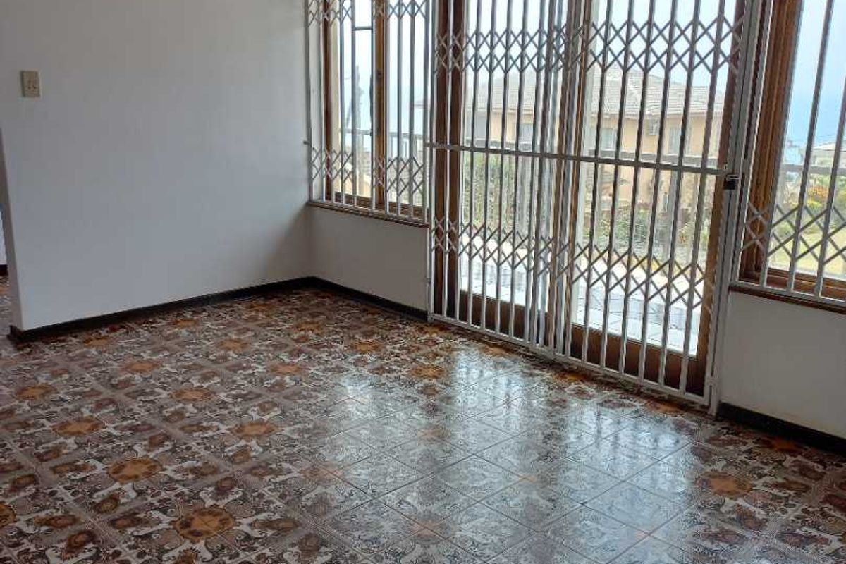 A bright, empty living room featuring patterned ceramic floor tiles, a timber-paneled ceiling, and large windows secured with metal security gates.