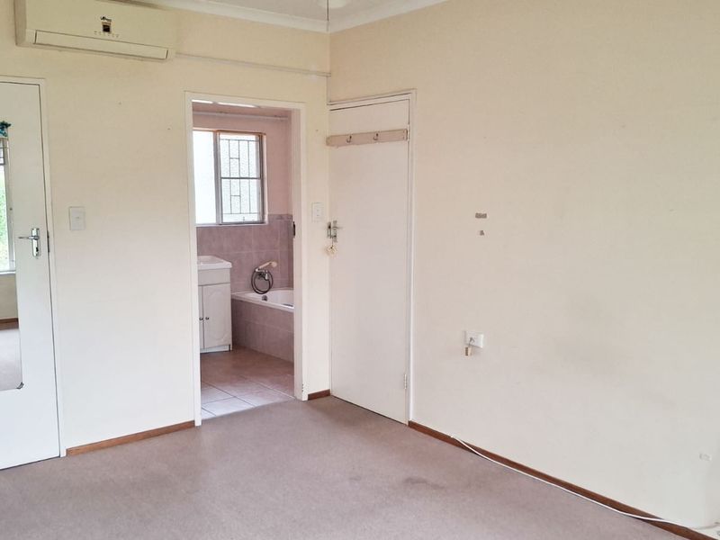 An empty bedroom featuring carpeted flooring, a split-system air conditioner, and direct access to an en-suite bathroom.