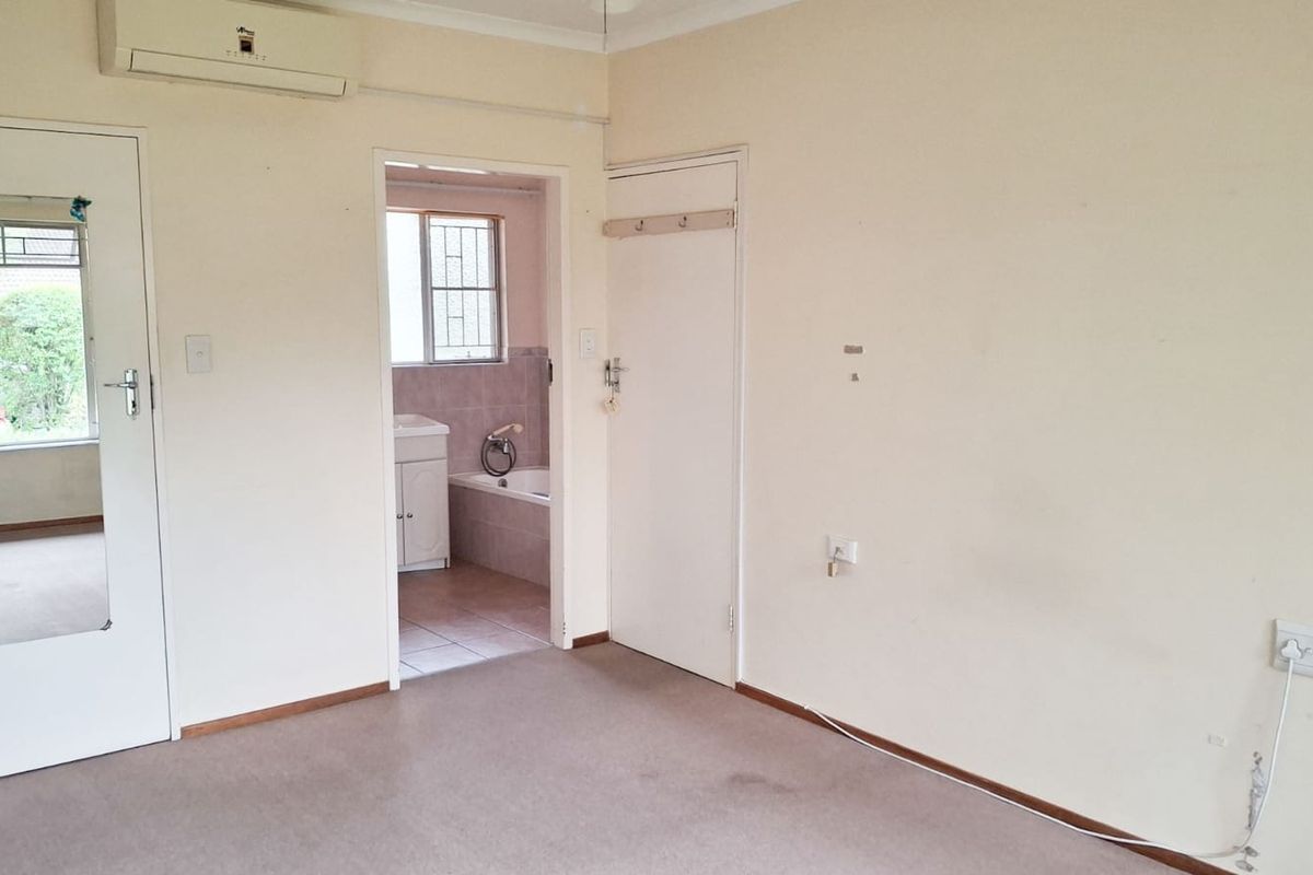 An empty bedroom featuring carpeted flooring, a split-system air conditioner, and direct access to an en-suite bathroom.