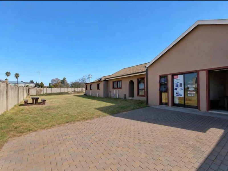Rear view of the property featuring a paved driveway, lawn area, and boundary wall, with access via sliding glass doors.