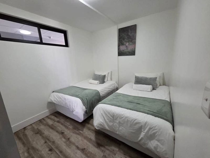 A compact bedroom featuring modern laminate flooring and a high-level window, providing a clean and functional sleeping space.