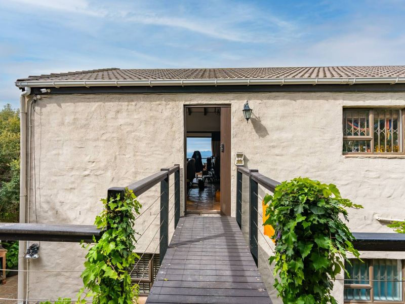 Rear exterior view featuring a timber footbridge leading to an entrance, with textured stucco walls and a tiled roof.