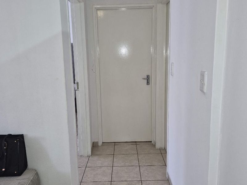 A clean and functional hallway featuring neutral tiled flooring and white interior doors, providing access to adjacent rooms within the apartment.