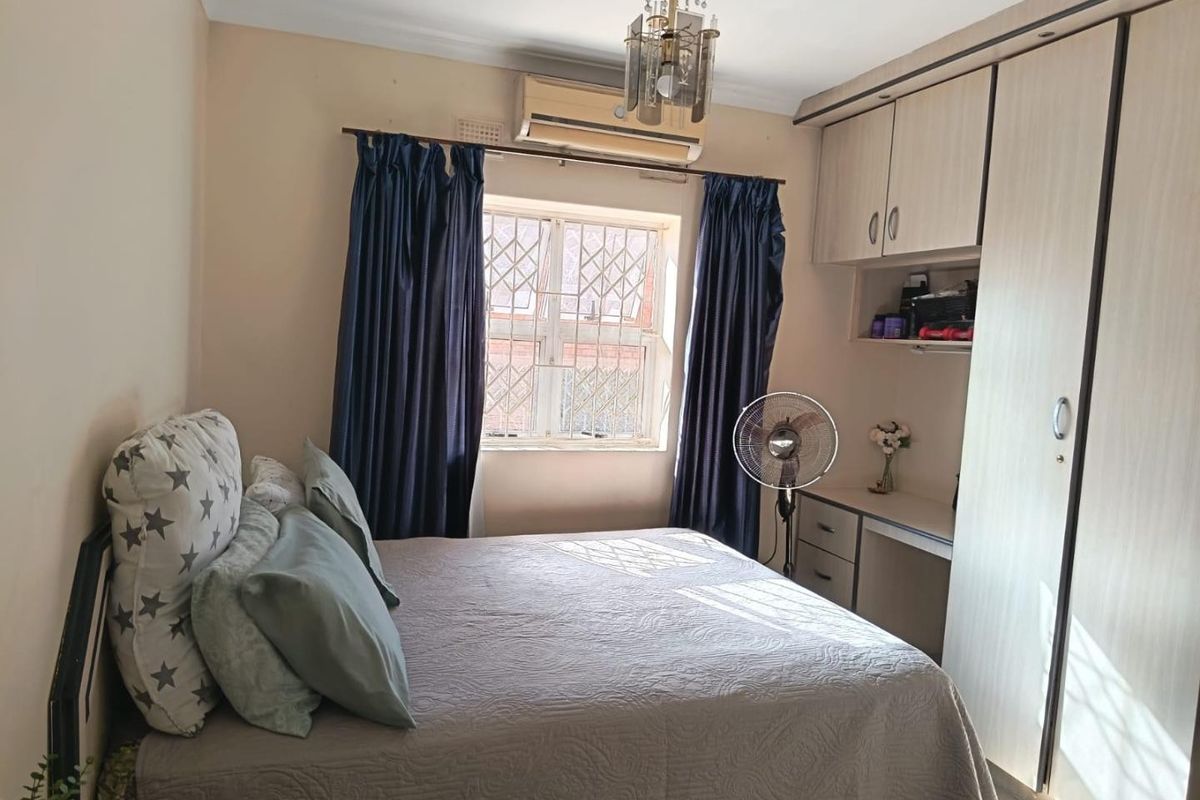 A functional bedroom featuring built-in cabinetry, a dedicated desk area, and a wall-mounted air conditioning unit.