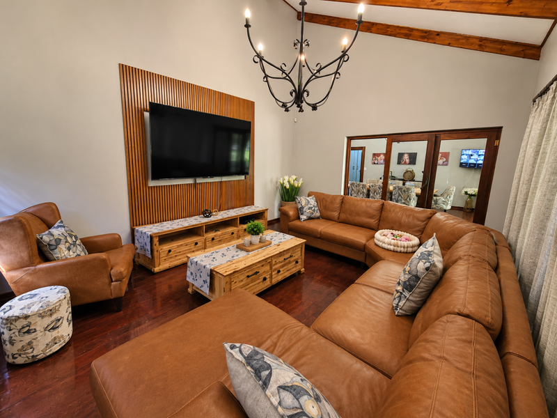 Spacious living room featuring a vaulted ceiling with exposed timber beams, a decorative timber slat feature wall, and warm hardwood flooring.