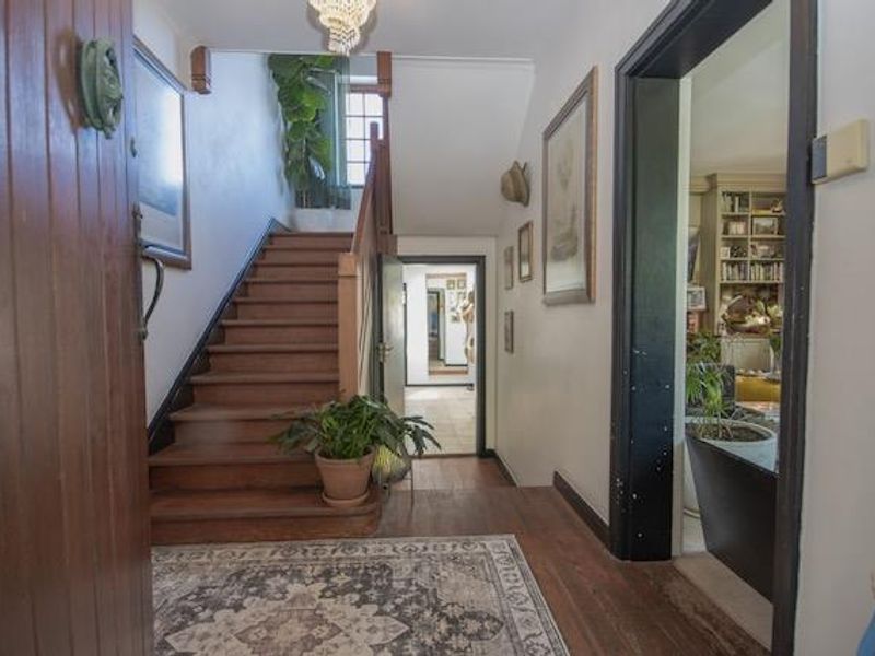 Welcoming entrance hall featuring a classic timber staircase, hardwood flooring, and a decorative chandelier, providing access to the main living areas.