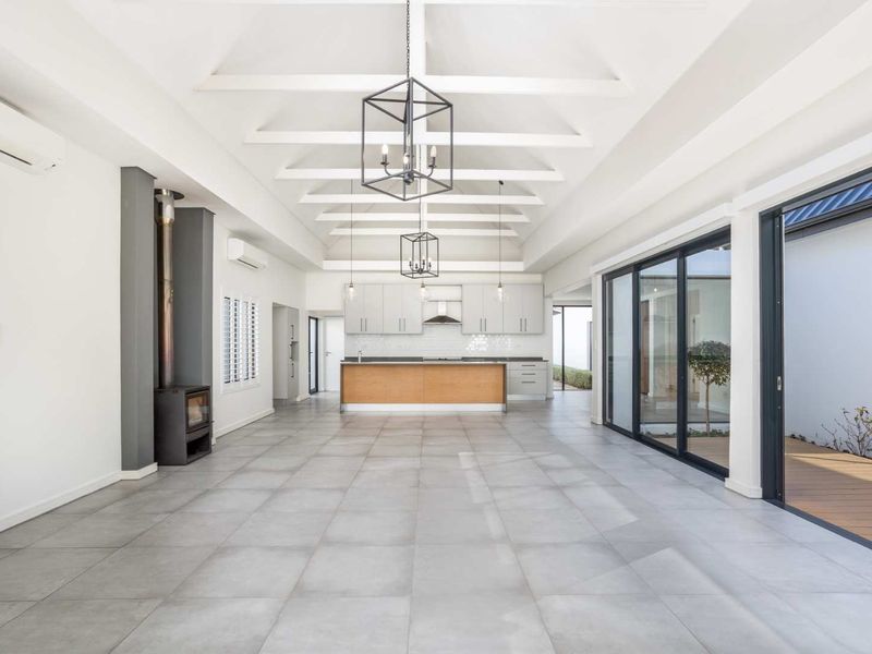 Spacious open-plan living and kitchen area featuring a vaulted ceiling with exposed beams, tiled flooring, a modern kitchen island, and a wood-burning fireplace.