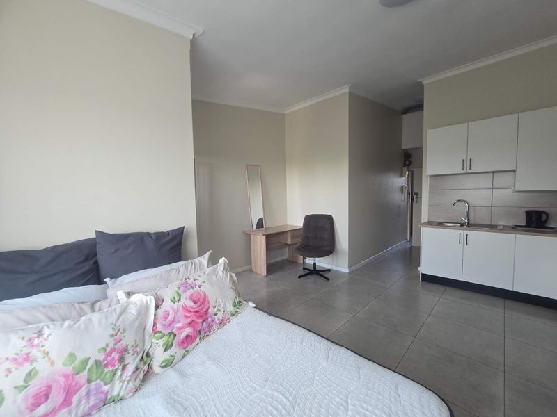 Open-plan studio apartment featuring a compact kitchenette with built-in cabinetry, stainless steel sink, and neutral tiled flooring throughout.