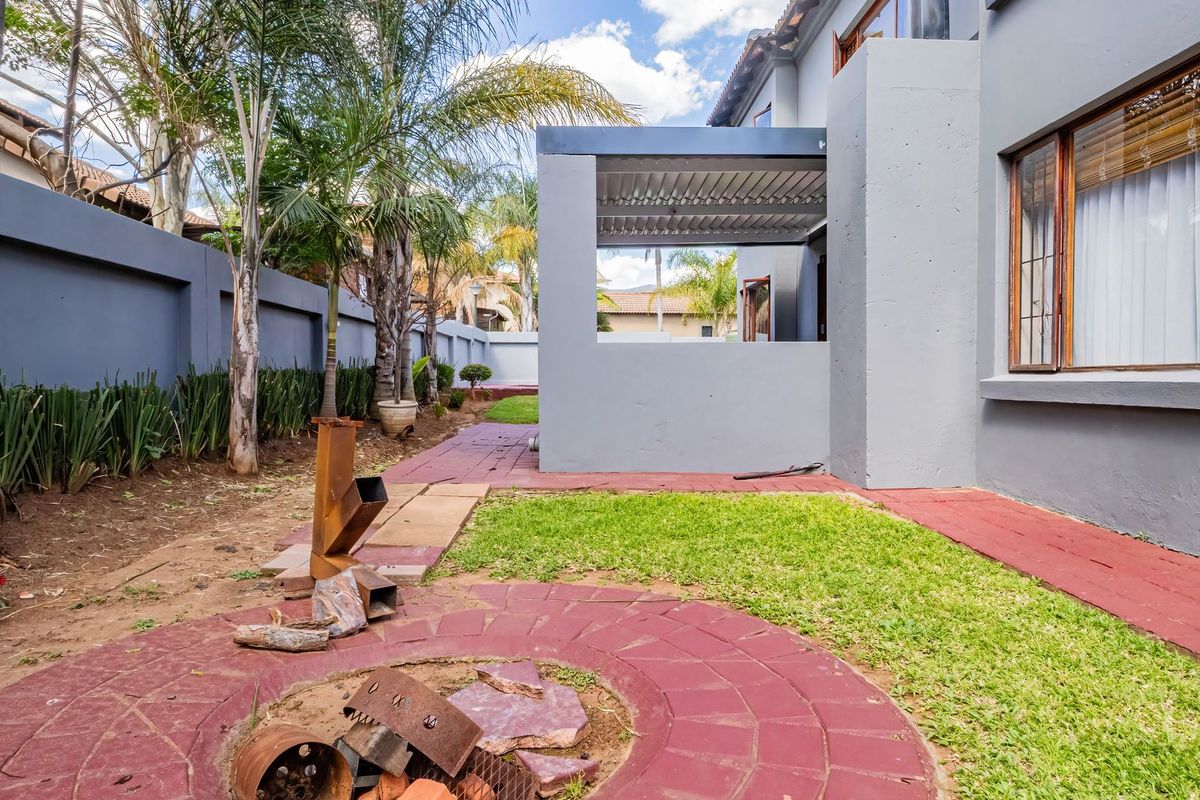 Rear garden area featuring a covered patio, paved walkways, and a built-in fire pit, enclosed by a perimeter wall.