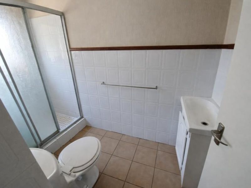 A functional bathroom featuring a shower enclosure, toilet, and vanity basin with tiled walls and flooring.