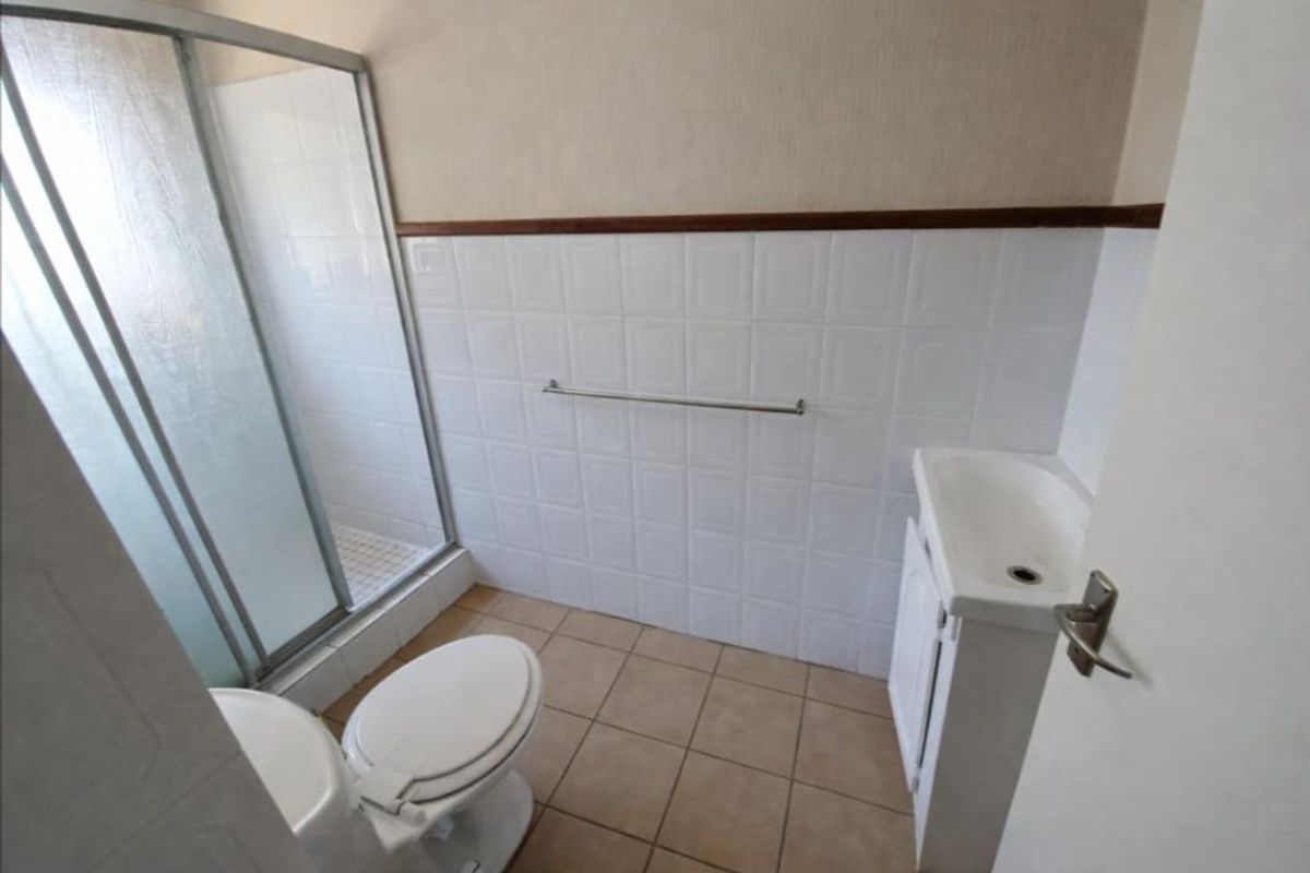 A functional bathroom featuring a shower enclosure, toilet, and vanity basin with tiled walls and flooring.
