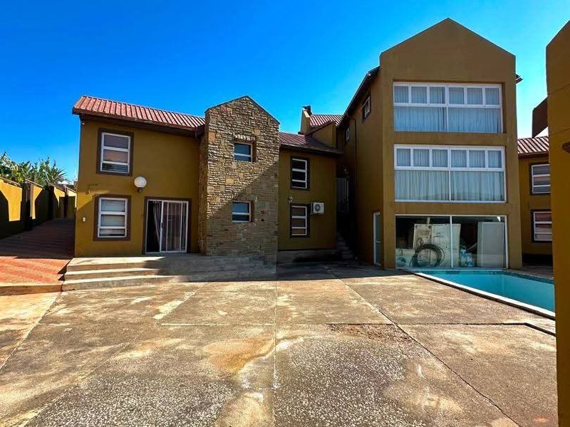 Rear exterior view of a multi-story house featuring a swimming pool, stone facade accents, and a large concrete patio area.