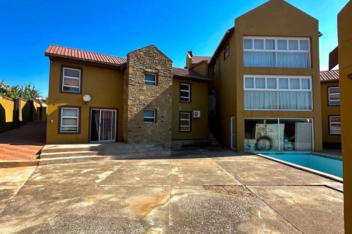 Rear exterior view of a multi-story house featuring a swimming pool, stone facade accents, and a large concrete patio area.