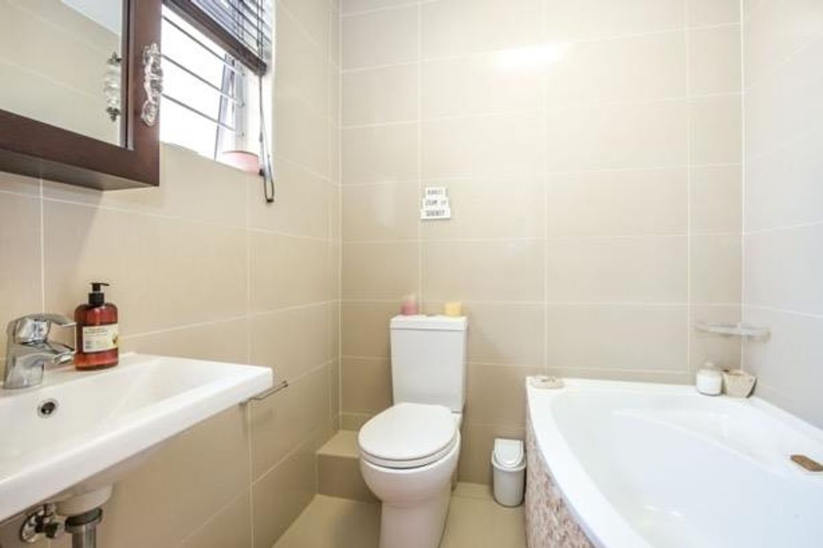 A compact bathroom featuring a white bathtub, a modern toilet, and a wall-mounted basin with tiled walls and flooring.