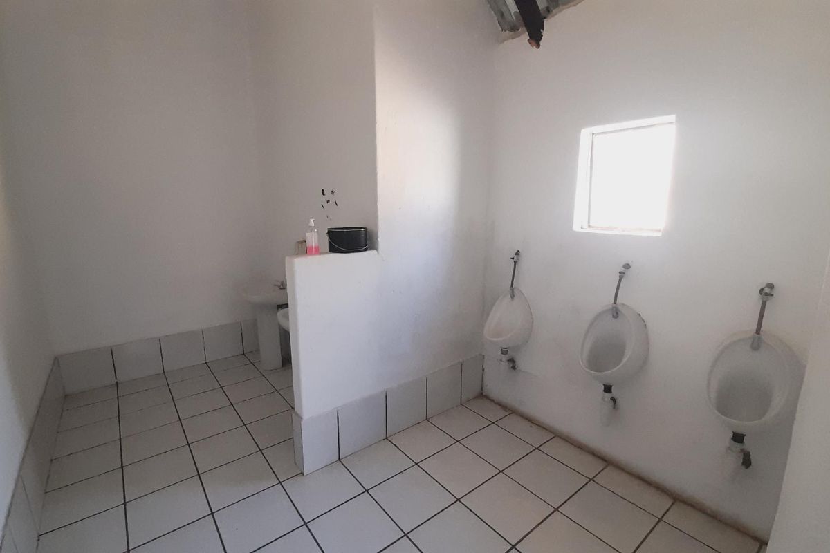 A functional commercial-style restroom featuring three wall-mounted urinals and a partitioned sink area with tiled flooring.
