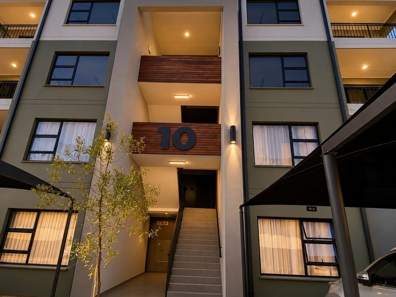 Modern apartment building facade featuring contemporary architectural design, paved driveway, covered parking, and well-maintained exterior finishes with integrated lighting.