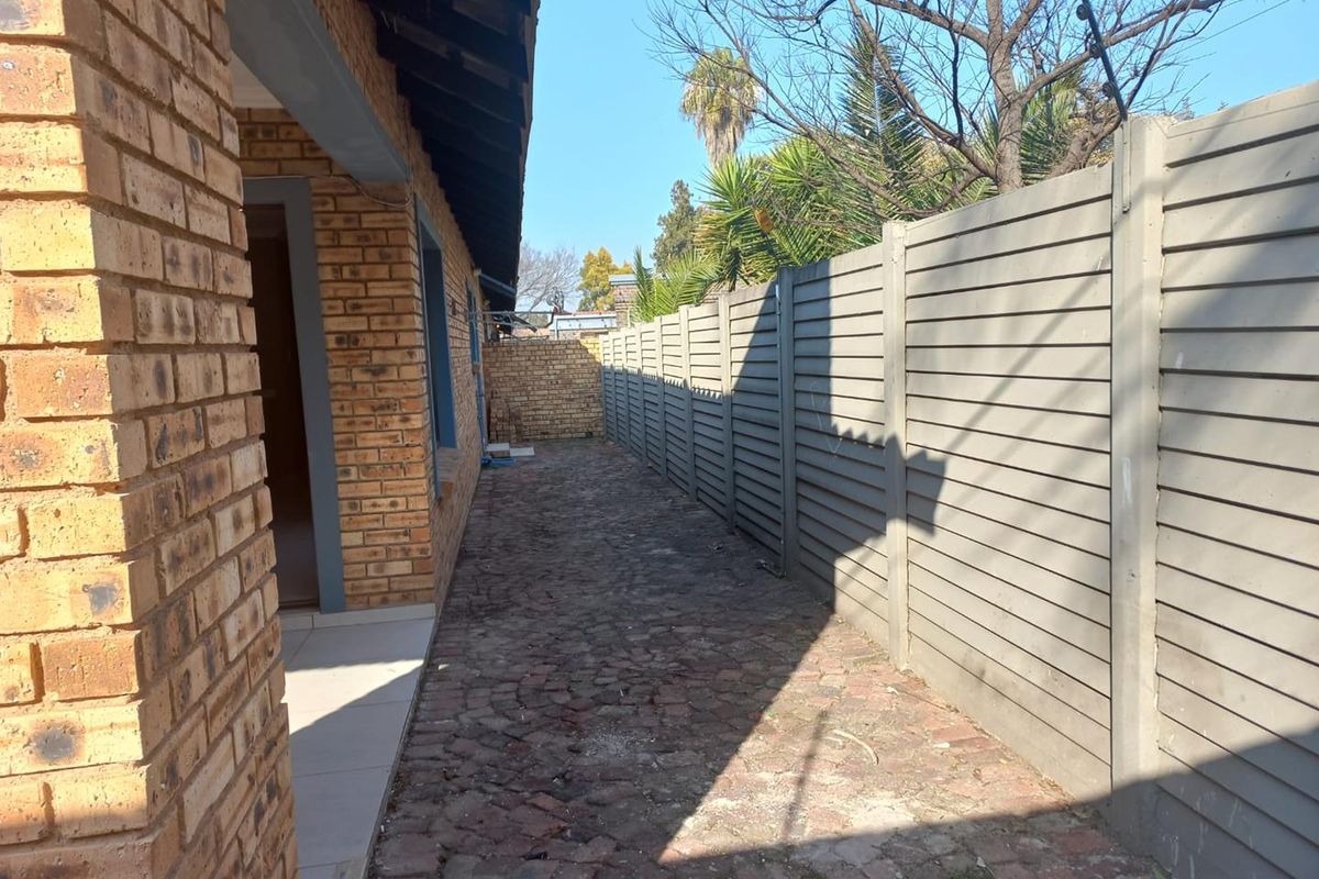 A side exterior walkway featuring face brick walling, cobblestone paving, and a precast concrete boundary fence.