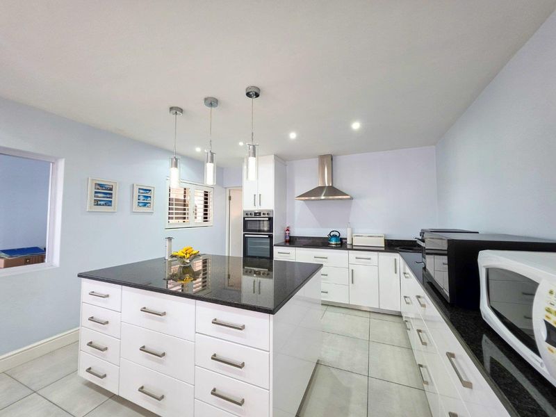 Modern kitchen featuring a central island with granite countertops, white cabinetry, built-in appliances, and contemporary pendant lighting.