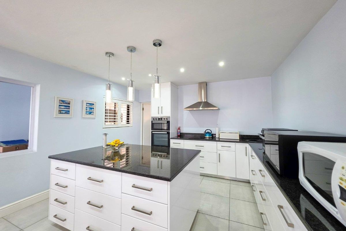 Modern kitchen featuring a central island with granite countertops, white cabinetry, built-in appliances, and contemporary pendant lighting.