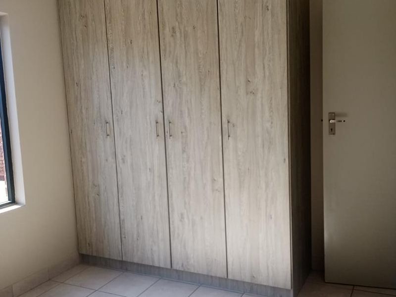 A bright, empty bedroom featuring modern wood-look built-in cupboards and neutral tiled flooring, offering a clean and versatile space.