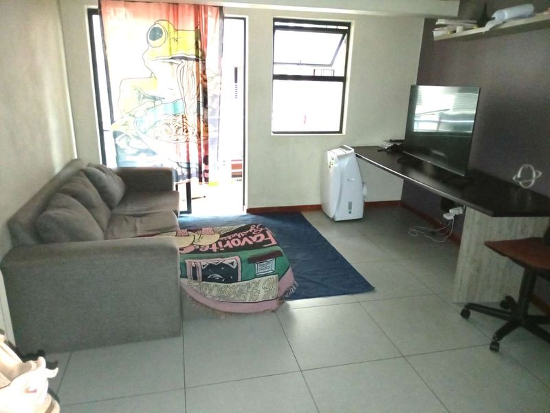 A living area featuring tiled flooring, a built-in desk, and access to an outdoor space through a sliding door.