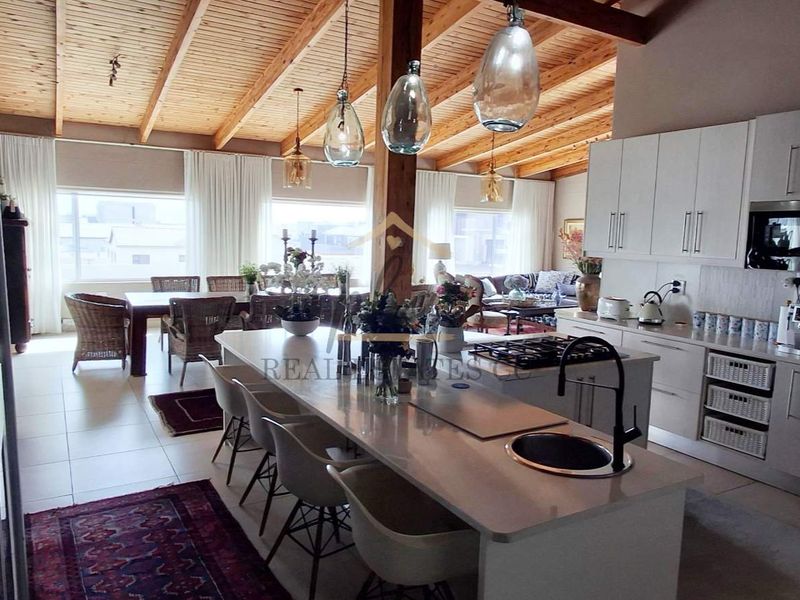 Spacious open-plan living and kitchen area featuring high exposed timber beam ceilings, a modern kitchen island with gas hob, and integrated appliances.