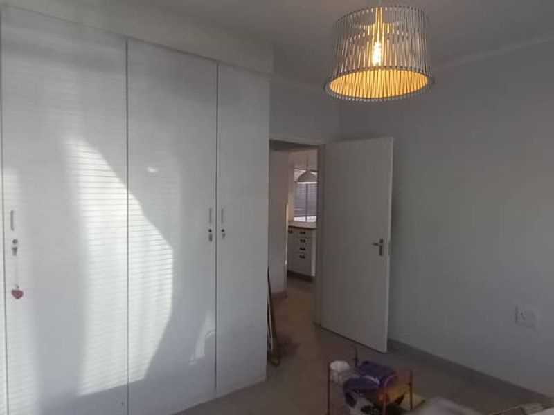 A bedroom featuring built-in cupboards, tiled flooring, and a pendant light fixture, with a view into an adjacent room.