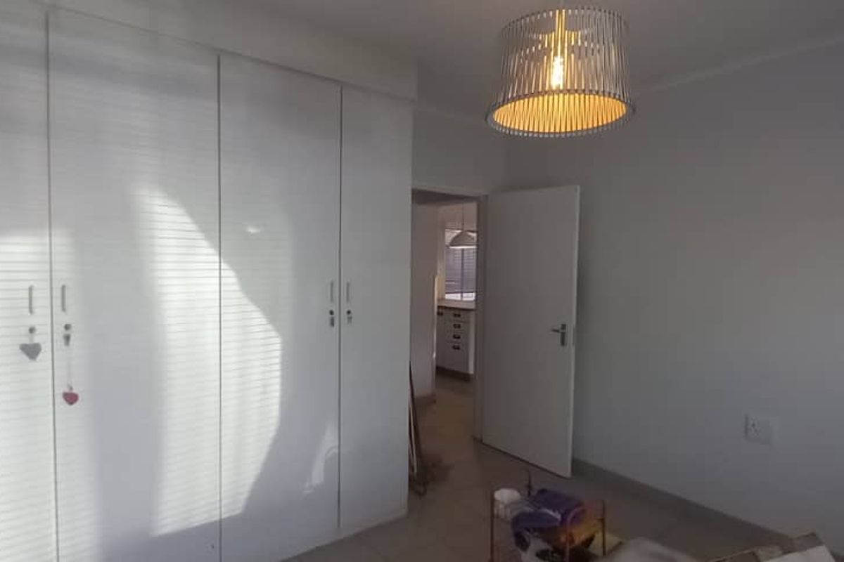 A bedroom featuring built-in cupboards, tiled flooring, and a pendant light fixture, with a view into an adjacent room.