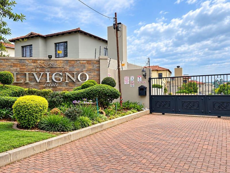 The entrance to Livigno Estate features a stone-clad signage wall, manicured landscaping, and a secure wrought iron gate with a paved driveway.
